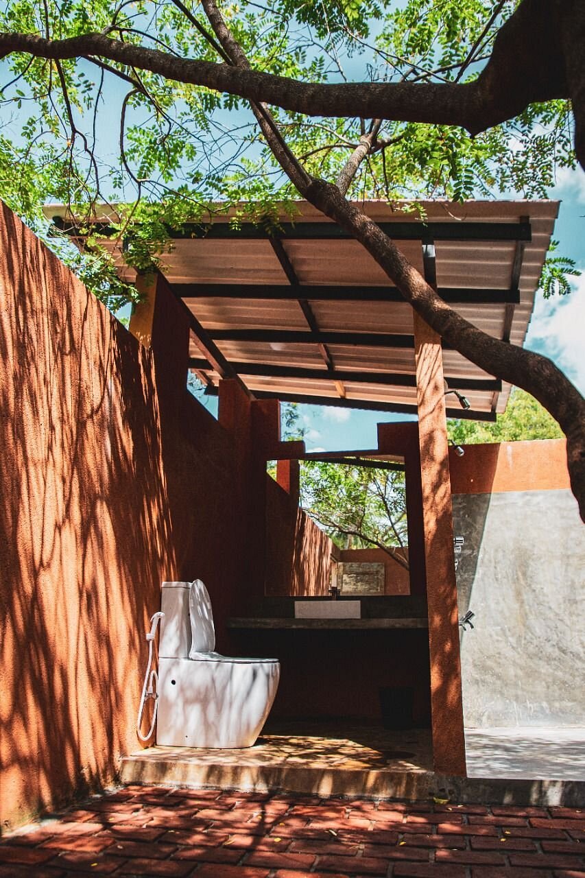 An outdoor bathroom at Ko Lake Villa featuring an open-air toilet, vanity, and shower under a tree canopy with natural light.