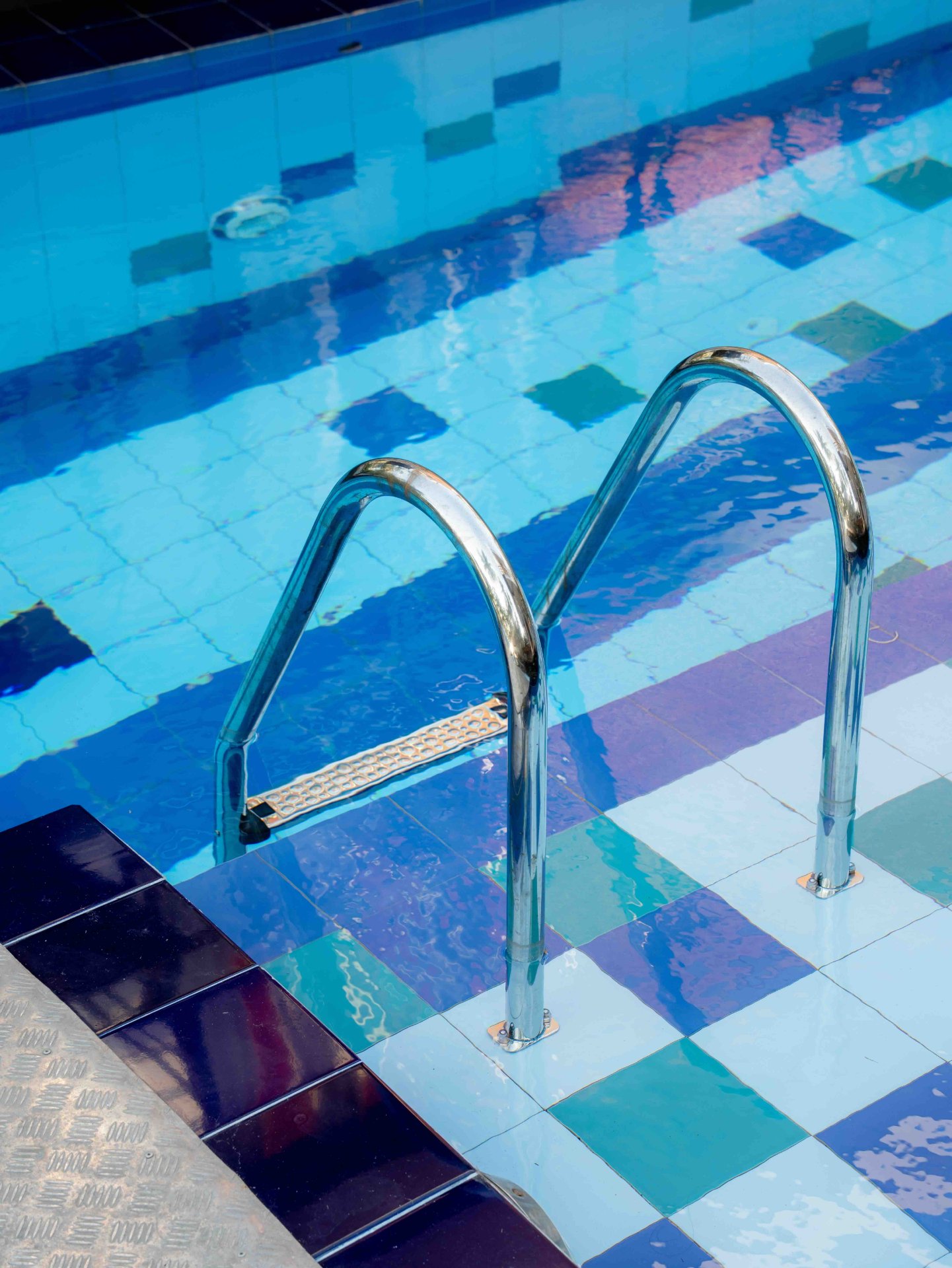 Close-up of bright blue pool steps and chrome handrails at Ko Lake Villa, reflecting the clear water.