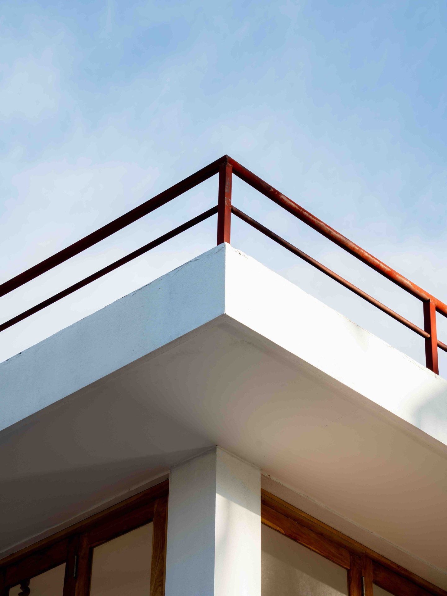 Ko Lake vista Balcony Edge - White Concrete & Red Railing - Ko Lake Villa boutique lakefront accommodation on Koggala Lake Sri Lanka: low-angle shot of a white concrete balcony edge with a vibrant red metal railing against a clear blue sky. Architectural detail.
