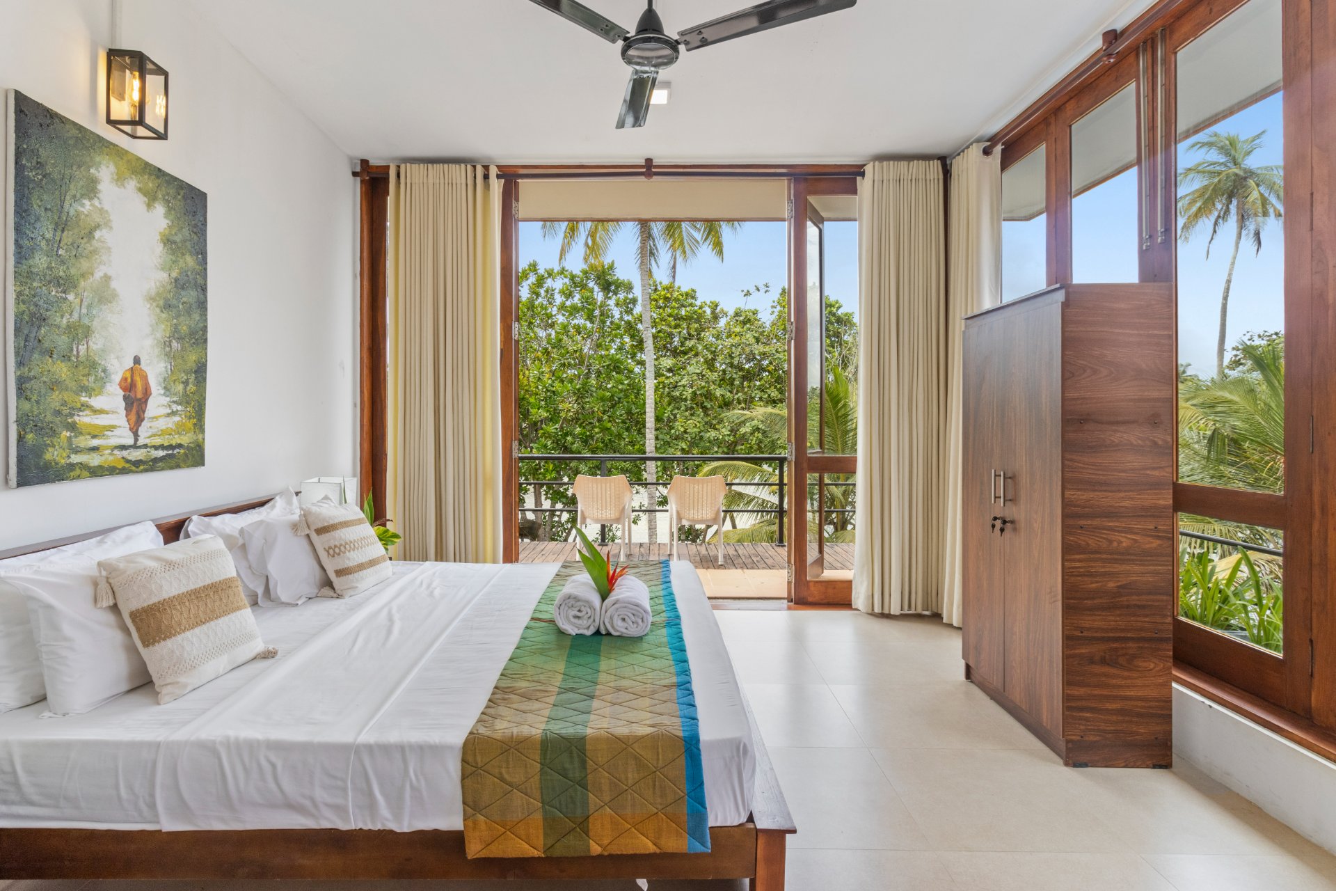 Tropica room r5 - Ko Lake Villa boutique lakefront accommodation on Koggala Lake Sri Lanka: Relax in this tranquil tropical bedroom. Featuring a comfy bed, balcony with seating, and stunning palm tree and garden views. Perfect for your next getaway!