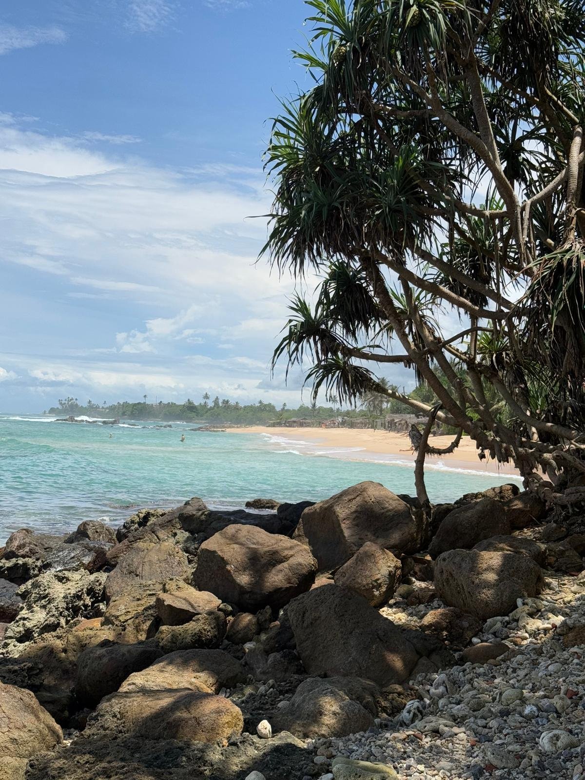 Scenic Rocky Beach with Turquoise Waters and Palm Trees in Ahangama - Ko Lake Villa boutique lakefront accommodation on Koggala Lake Sri Lanka: Explore a beautiful tropical beach featuring clear turquoise ocean, large rocks, and lush palm trees under a bright blue sky.