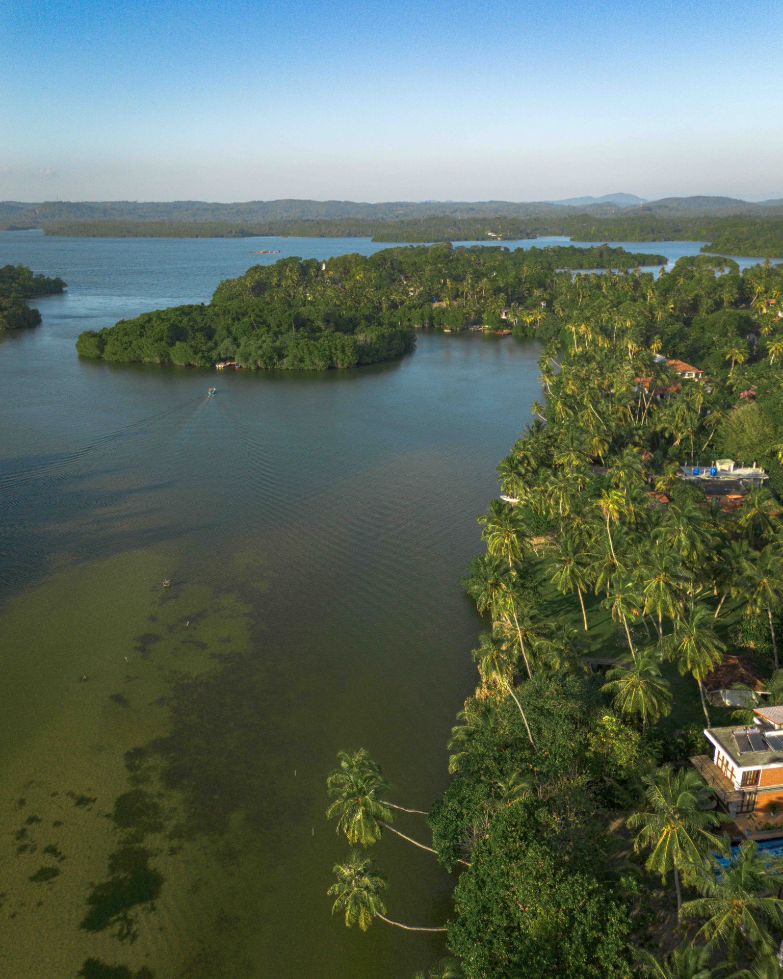 Aerial View: Koggala Lake Palm-Lined Shores - Ko Lake Villa boutique lakefront accommodation on Koggala Lake Sri Lanka: Stunning drone view of Ko Lalke on the right of the frame, with lush tropical showers, winding through islands and palm-covered shores. Perfect for nature, travel, and landscape enthusiasts.