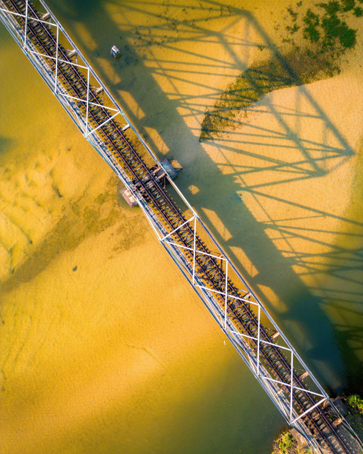 Aerial View: Koggala Railway Bridge Over Shallow Water & Sand - Ko Lake Villa boutique lakefront accommodation on Koggala Lake Sri Lanka: Stunning aerial shot of a long railway bridge spanning shallow, sandy water. Unique shadows, industrial architecture, and natural patterns.